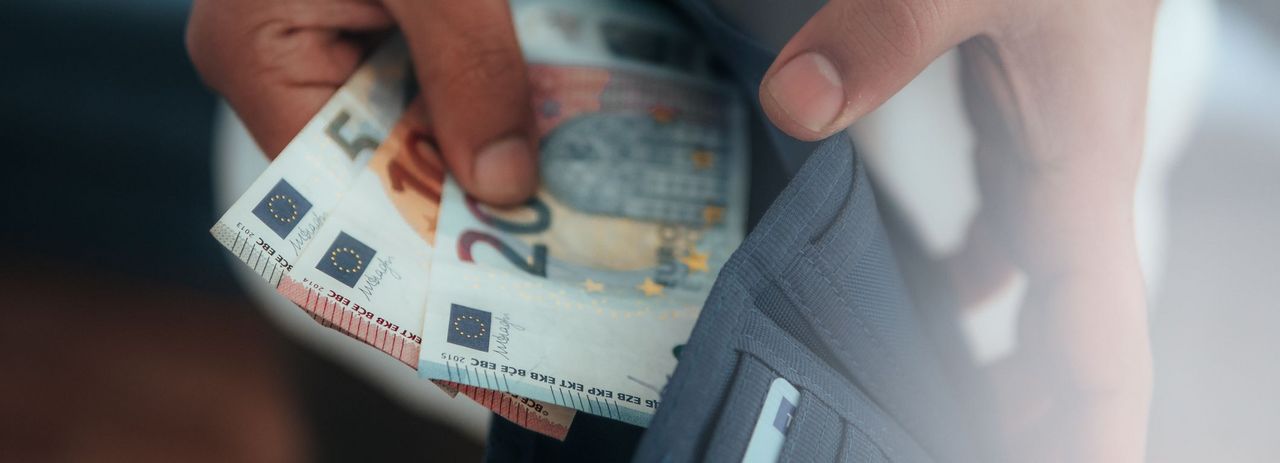 Ein Mann nimmt Geldscheine aus einem Geldbeutel.